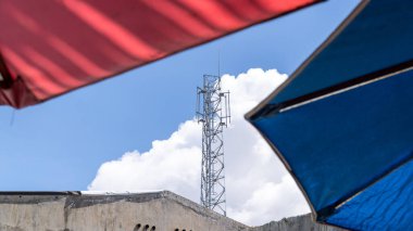 Açık mavi gökyüzüne uzanan uzun iletişim kulesi, renkli kırmızı ve mavi gölgelerle çerçevelenerek telekomünikasyon ve inşaat temaları için uygun hale getiriliyor..