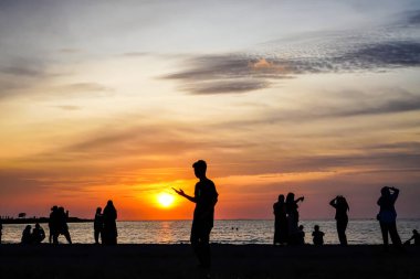 Siluetli insanlar büyüleyici bir günbatımında sahilde toplanıp seyahat ve tatil temalı içerik için mükemmel sıcak ve davetkar bir sahne yaratıyorlar..