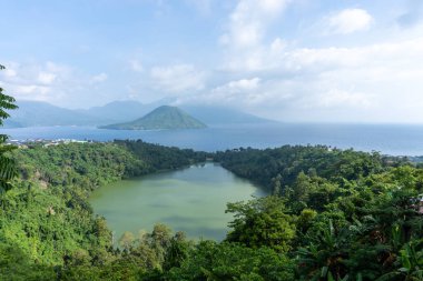 Yoğun tropikal ağaçlar ve uzaktaki okyanusla kaplı, seyahat ve doğa yayınları için uygun, dingin bir göl manzarası..