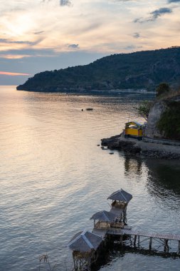 Günbatımı tropikal kıyıları kulübeyle ve dağlarla kaplıyor. Yumuşak bir ışık altında cennet gibi bir ada kaçamağı ilhamı ve turizm pazarlaması için..