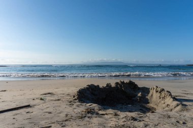 Bir kumdan kalenin kalıntıları, arka planda okyanus dalgaları olan kumlu bir sahilde oturur. Sahil yolculuğu ya da tatil teması için mükemmeldir..