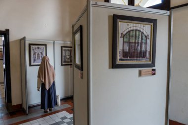 Başörtüsü takan bir kadın, kapalı bir sanat sergisinde çerçeveli mimari çizimler yapar. Kültürel etkinlikler ve seyahat promosyonları için mükemmeldir..