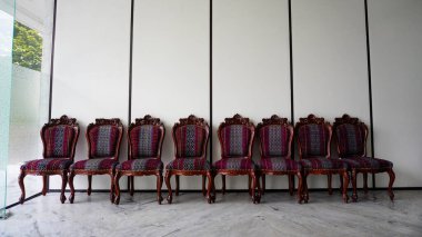 Mobilyalı döşemeleri olan yedi süslü ahşap sandalye, mobilya ve iç tasarım projeleri için mükemmel beyaz panelli bir duvara karşı oturur..