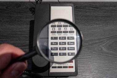 Eski bir otelin telefon tuş takımının üzerinde, konukseverlik ve teknoloji kavramları için mükemmel detaylar ve potansiyel konuların vurgulandığı bir büyüteç tutan el..