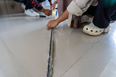İnsanlar fayans zeminindeki bir boşluğa bant yapıştırıyor, yenileme veya onarım sürecini gösteriyor, DIY ve inşaat temaları için uygun.