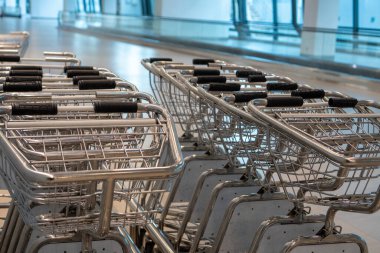 Havaalanı terminalinde dizilmiş parlak metal bagaj arabaları yolculara ve eşyalarına yardım teklifinde bulunuyor. Bunu ulaşım teması olarak düşünün..