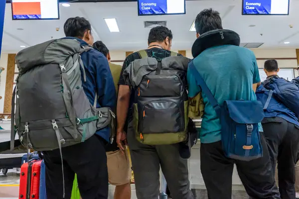 Birkaç yolcu, seyahat için hazır sırt çantaları ve bavullarıyla kontrol gişesinde duruyor ve seyahat içeriği için uygundur..