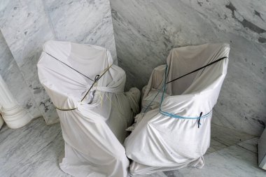 Renkli iple bağlanmış beyaz kumaşla örtülü iki sandalye mermer zeminde, yenilenme ve dizayn teması için mükemmel bir şekilde kapalı duruyor..