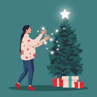 Konforlu kış giysileri içindeki genç bir kadın Noel ağacını çelenkle süsleyecek. Noel ve Yeni Yıl hazırlığı kavramı.