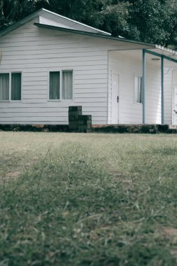 Bahçesinde çimen olan beyaz ahşap bir ev ve kırsal kesimdeki evin arkasındaki ağaçlar. Bu fotoğraf, mimil ve batı Kalimantan renklerinde kurbağa gözleriyle çekilmiş.        