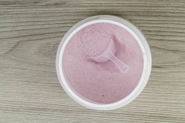 Protein tozu kepçeyle plastik kavanozda, ahşap arka planda, üst tarafta, düz yerde.