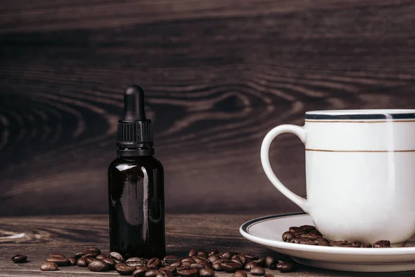 vintage cup of coffee with roasted beans and bottle with cbd oil or essential oil on wooden backround