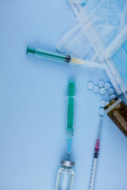 Beyaz koruyucu eldiven, tıbbi maske, iğneli şırınga, aşı şişesi ve haplar. Spor konseptinde yasadışı doping, grip aşısı, uyuşturucu bağımlısı, ıslak tıp. tıbbi öge arkaplanı