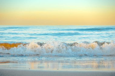 Tropical light blue water with waves at a white sand beach and orange and yellow colorful sky in a colorful Mediterranean sunset