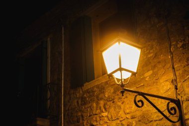 Karanlık ortaçağ şehrinde parlayan eski sokak lambası taş duvarda.