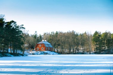 Traditional idyllic Swedish red wooden timber cabin house paint with falu red paint in winter landscape with frozen lake