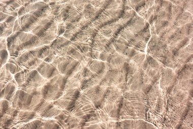 Şeffaf suyun altında beyaz kum deseni. Güneşin yansıması cennetten gelen küçük dalgalar halinde.