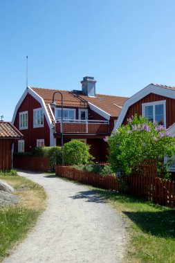 Stockholm Takımadaları 'nda mavi gökyüzü ile aydınlık bir yaz gününde, huzurlu kırsal alanda beyaz köşeli iki İsveç kırmızı boya evine giden dar çakıl yolu.