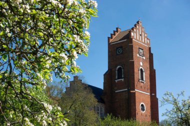 İsveç, Vadstena 'daki Rodtornet kırmızı kilise kulesi baharda yeşil ve çiçek açan ağaçla