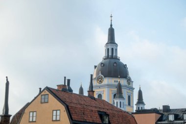 Sarı boyalı İsveç Kubbesi Kilisesi. Sabah Katarina Kyrka. Ön planda sarı sanayi dönemi yerleşim binaları var.