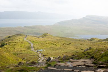 Yazın İskoçya 'nın Skye Adası' nın arka planında yeşil tepelerin ve dağların üzerinden geçen yürüyüşçülerle dolu bir patika ve doğa yürüyüşü.