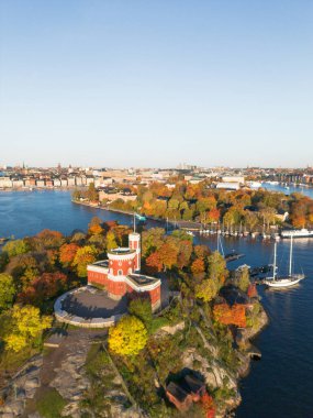 Kastellholmen, İsveç 'te sarıya ve portakal ağaçlarına dönüşen güneşli bir sonbahar sabahında arkasında Stockholm silueti olan adada kırmızı şato.