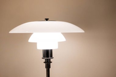 Kopenhag, Danimarka - 28 Aralık 2024: Zarif Louis Poulsen PH geleneksel opal masa lambası Poul Henningsen tarafından tasarlanan sıcak bej duvar arka planına karşı Danimarka iç tasarım konsepti.