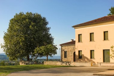 Yazın, sıcak öğleden sonra güneşinde, Chiesa Parrocchiale dei Santi Nazario e Celso - Vo Euganeo 'daki Cortel Kilisesi' nde, eski taş evlerin yanında büyük bir ceviz ağacı olan İtalyan kırsal meydanı.