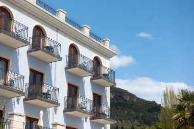 Sal, İtalya - 8 Nisan 2025: Lüks 5 yıldızlı Bellerive Lifestyle Oteli 'nin balkonlu dış ve mavi cephesi Palmiye ağaçları ve dağlarla kaplı arka planda Lago di Garda Gölü