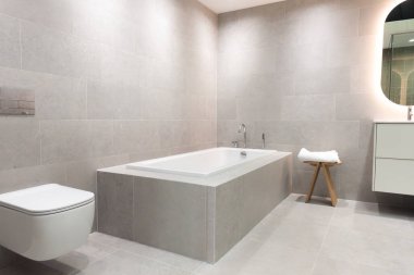 Modern seramik küvet paslanmaz çelik ve krom musluklarla modern bir banyoda gri fayanslı duvarlar ve zarif ev dekorasyonu için zemin