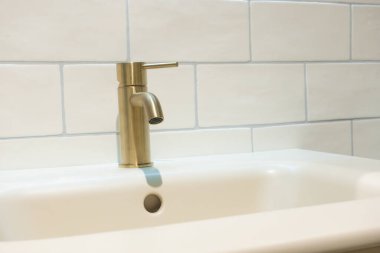 Krem beyaz fayanslı beyaz bir banyo konsepti ve antika bir pirinç musluk ve beyaz bir leğeni tıkırdatma