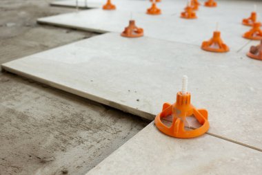 Turuncu takozlar ve uzaylılarla profesyonel bir kiremit seviyelendirme sistemi kullanılarak seramik zemin fayanslarının yakın görüntüsü