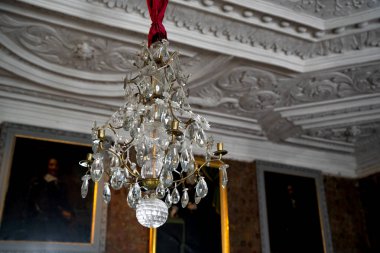 Closeup of crystal chandelier pendant lamp in aristocratic home with decorative plaster ceiling painted portraits on the walls in the background