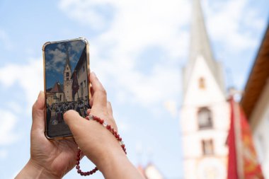 tourist taking a photo of a group of people wearing traditional south tyrolean costumes in front of Santa Cristina church in Val Gardena, Italy, during annual annual summer Ladin heritage festival
