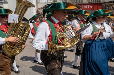 Santa Cristina (BZ), Italy - 20 July 2025: Man playing a French horn in a folk marching band wearing a traditional south tyrolean tracht and lederhosen during a procession festival in Val Gardena