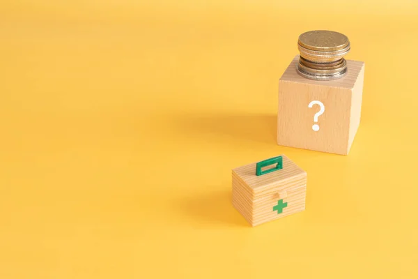 Medical expenses; A wooden block with a question mark, coins, and a first aid box.
