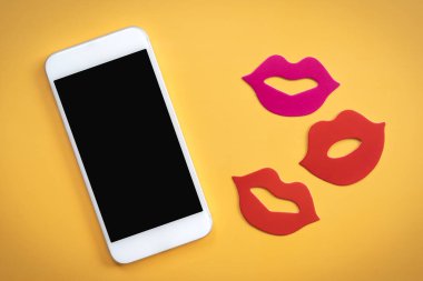 Parlak sarı arkaplanda kırmızı dudakları olan siyah bir cep telefonu ekranı.  