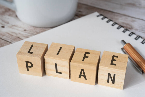 Wooden blocks with "LIFE PLAN" text of concept, a pen, a notebook, and a cup.