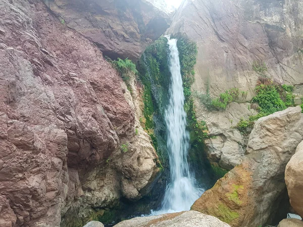 A refreshing waterfall in the Moroccan mountains. The waterfall cascades down a rocky cliff into a pool of clear water. The photo captures the beauty and serenity of the natural setting