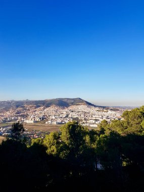 Doğanın şehir manzaralarına kuş bakışı bakış, bu nefes kesen fotoğrafla ormanın üzerinde süzülür, canlı şehir manzaralarını yakalar, güneş ışınları genişleyen şehir gökyüzünü aydınlatır, sonsuzluk hissi verir.