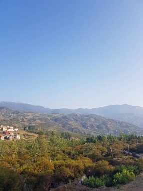 Zirveli bir dağ sırası. Dağlar yuvarlanan tepeler ve yemyeşil ormanlarla çevrilidir. Güneş ışıl ışıl parlıyor, gökyüzünde güzel bir altın parıltısı yaratıyor.