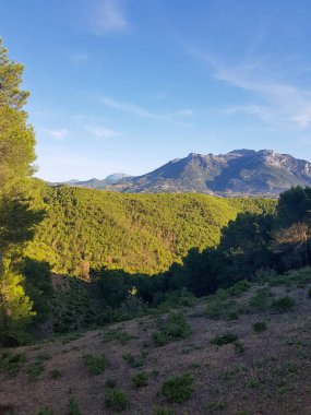 Doğal bir manzaradaki görkemli dağ sıraları uzun ve kayalıktır. Manzara gür ve yeşildir. Görüntü doğal ışık altında alınır ve dağların, manzaranın ve gökyüzünün detaylarını gösterir.