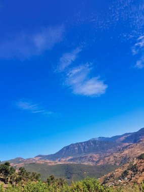 A breathtaking view from a hilltop, where rugged mountain peaks stretch toward the sky. The landscape is adorned with lush greenery, winding trails. Sunlight filters through the mist. clipart