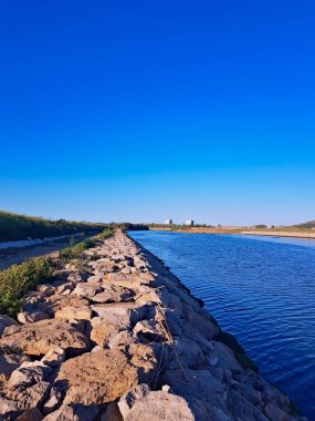 A serene wadi scene with a natural rock arrangement on the left. The sky above is painted in soothing blue hues, creating a breathtaking reflection in the calm waters. As the day draws to a close. clipart