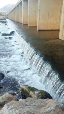 Vadideki bir köprünün altında geniş bir dere. Akan suya yakın çekim, karmaşık ayrıntıları ortaya çıkarıyor