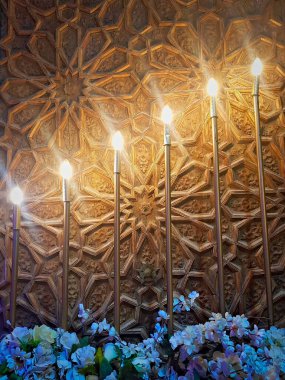 Işıklar arka planda oyulmuş ahşap ve çiçeklerle düzenlenmiş.