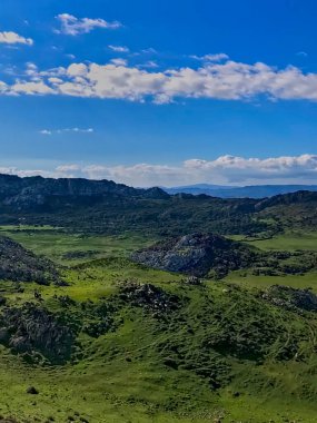Görkemli dağ tepeleri, bereketli yeşillik ve canlı vahşi yaşamla süslenmiş engebeli dağlar. Işık ve gölgenin etkileşimi dinamik bir atmosfer yaratır..