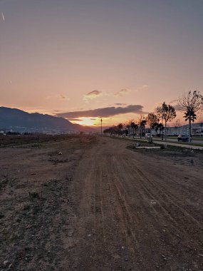 Gün batımında asfalt bir yolun kenarına kurulmuş çakıllı bir yol pitoresk bir akşam sahnesi yaratır..