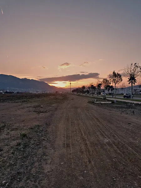 Gün batımında asfalt bir yolun kenarına kurulmuş çakıllı bir yol pitoresk bir akşam sahnesi yaratır..