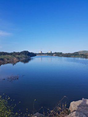 Huzurlu bir göl, akşam gökyüzünün altında, çevresindeki manzarayla güzelce çerçevelenmiştir. Sakin atmosferi, doğanın gerçek özünü yakalar..